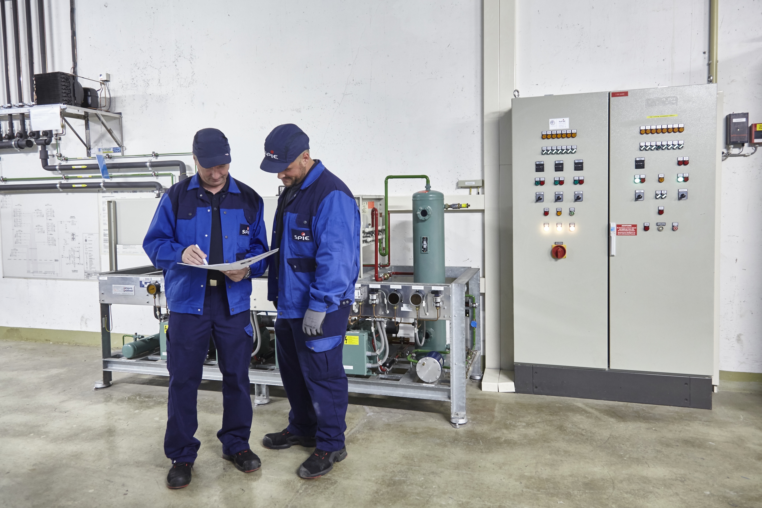 Bild von zwei männlichen Technikern während einer Besprechung in einer Halle vor technischen Anlagen - Bildnachweis: SPIE